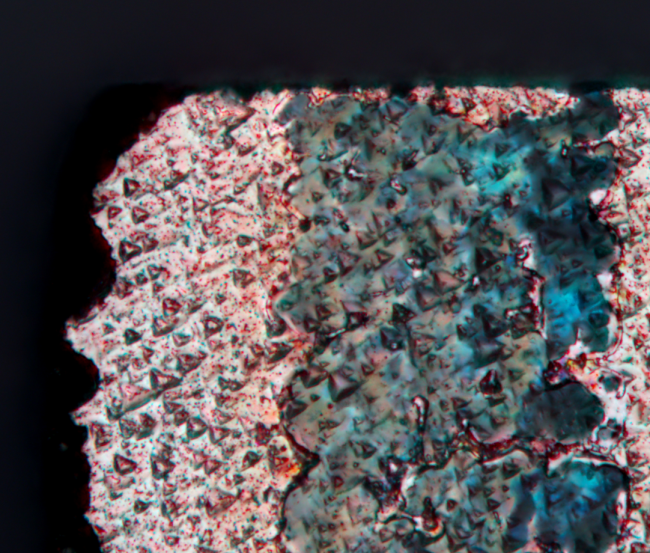 An unknown object with a rough surface made of small pyramids. Colours and shapes remind of an aerial image of a desert or an alien planet.